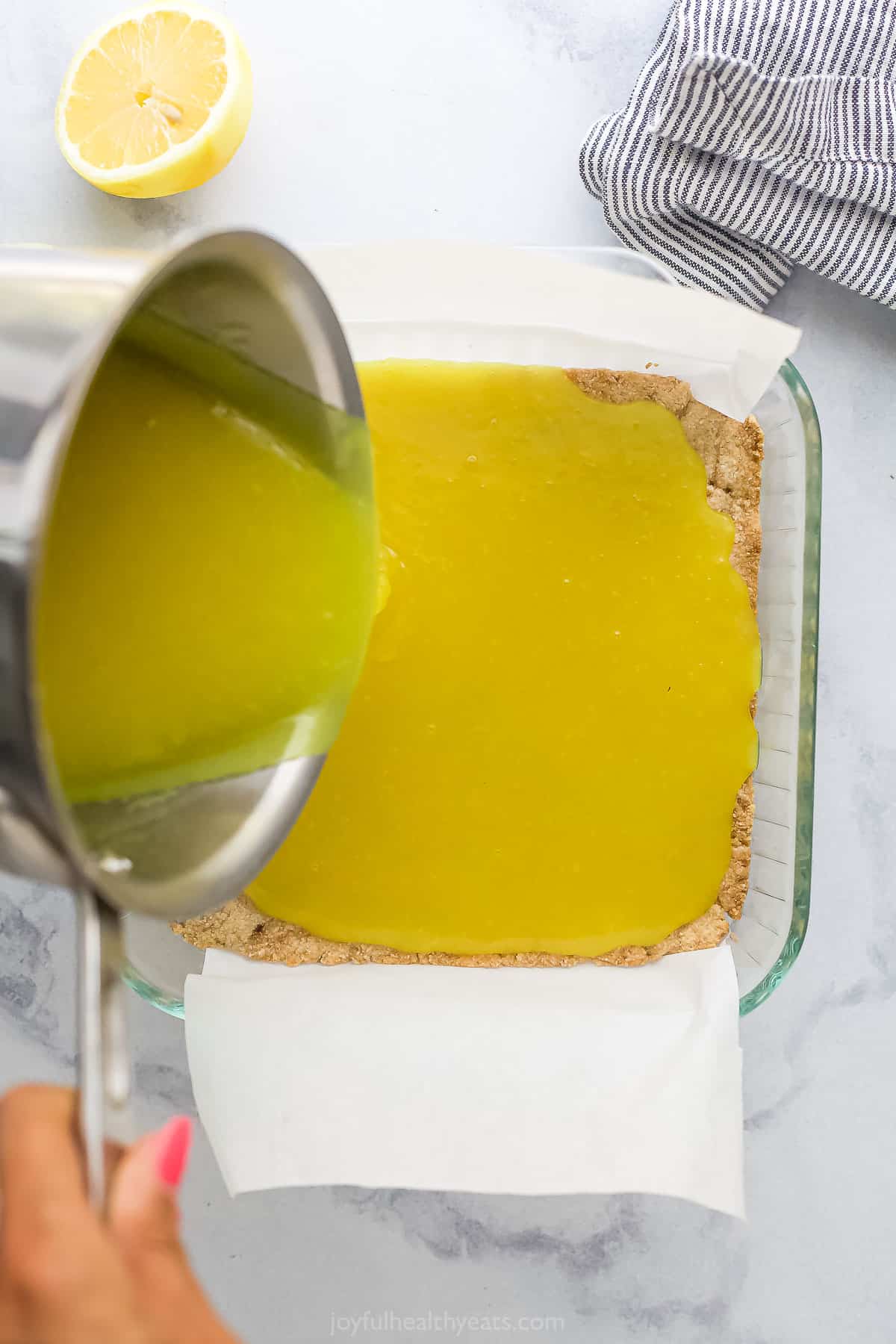 Lemon curd filling being poured over a maple almond crust in a glass baking dish