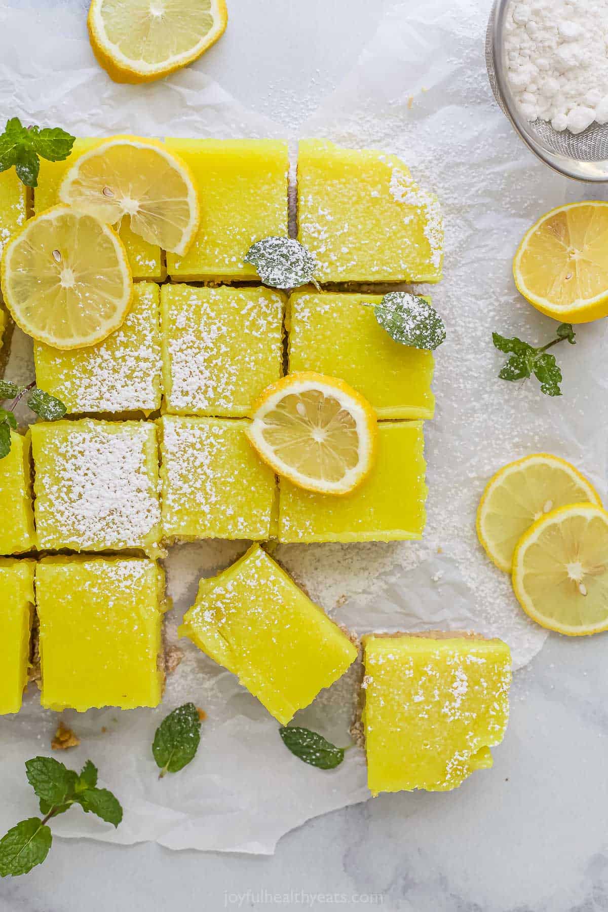A bunch of homemade lemon squares on a piece of parchment paper on top of a marble countertop