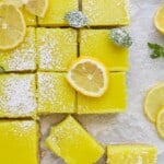 A batch of vegan and gluten-free lemon squares on a countertop with fresh mint leaves and lemon slices