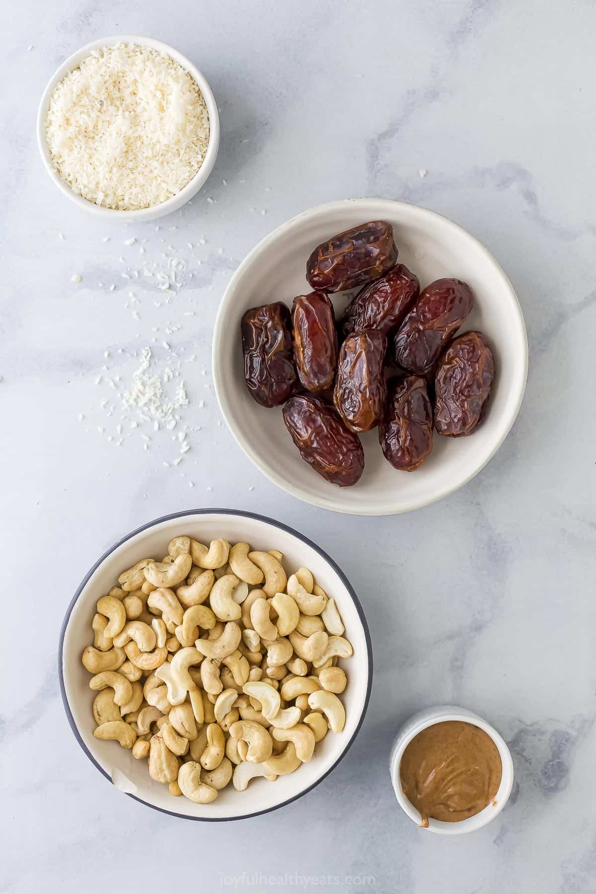 Whole dates, unsweetened shredded coconut, cashews and almond butter on a marble countertop