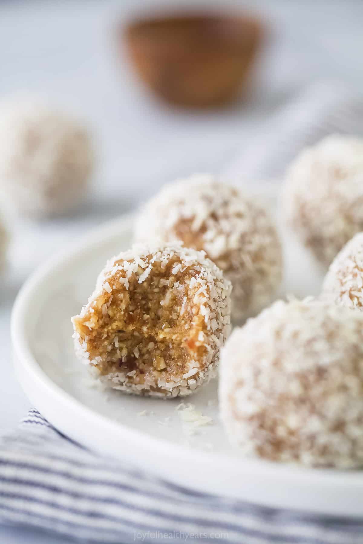 A close-up shot of coconut protein bites on a plate with the one in focus missing a bite