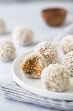 A bunch of coconut bliss balls on a plate with a bite taken out of one of them