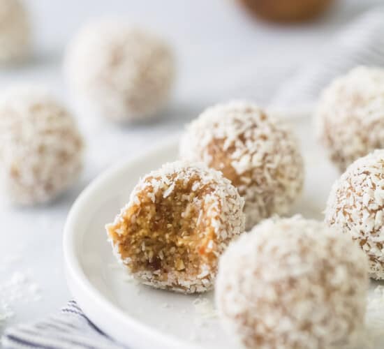 A bunch of coconut bliss balls on a plate with a bite taken out of one of them