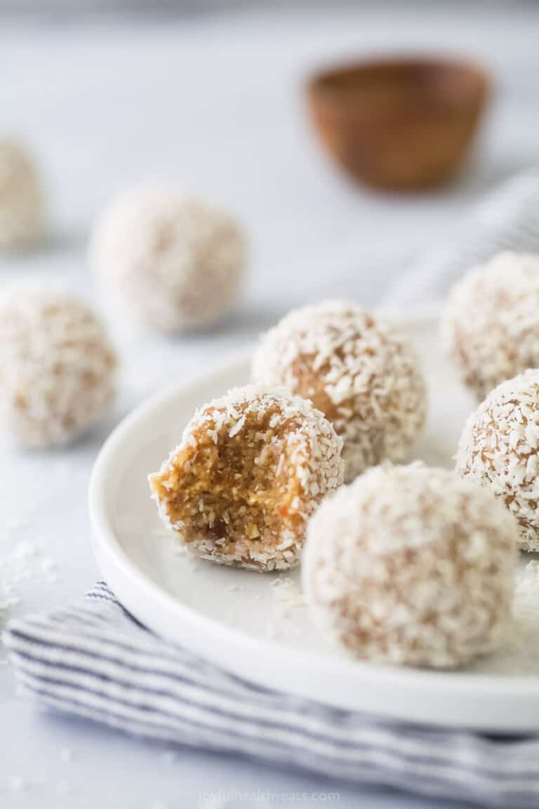 A bunch of coconut bliss balls on a plate with a bite taken out of one of them