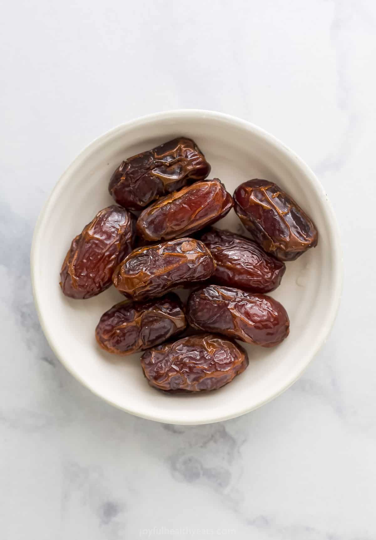 A small white dish holding nine whole dates