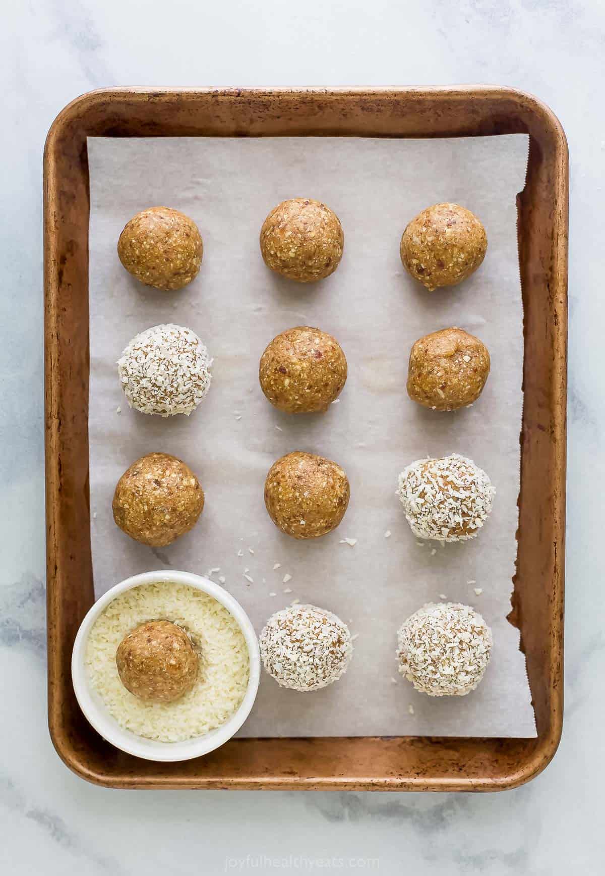 A batch of bliss balls in the process of being coated in shredded coconut on a lined baking sheet