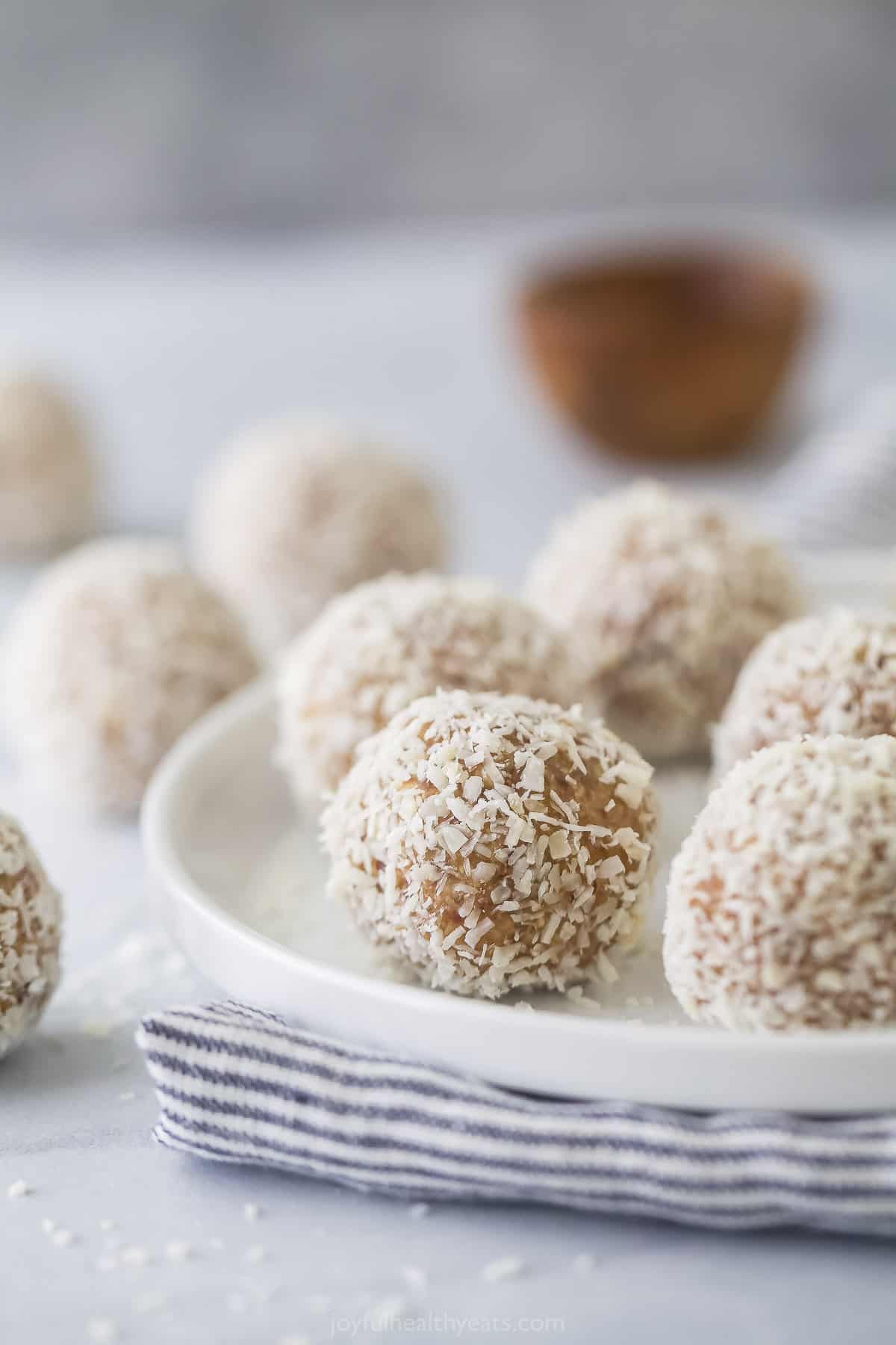 Coconut bliss balls on a plate on top of a striped dishtowel