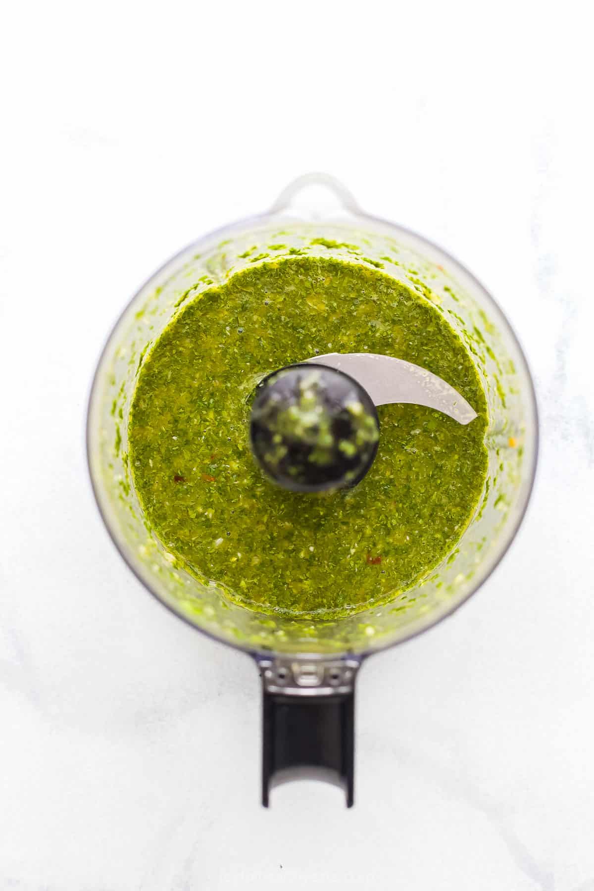 Homemade chimichurri dressing inside of a food processor on a marble countertop