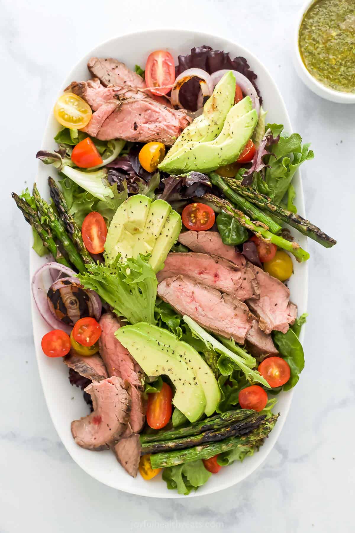 A beef avocado asparagus salad on a rectangular platter on top of a marble surface