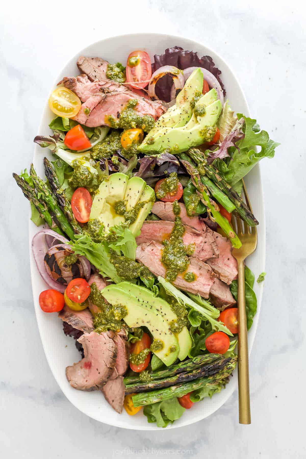 California steak salad with chimichurri dressing on a serving platter with a golden fork
