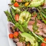 A platter of California steak salad topped with a drizzle of chimichurri dressing