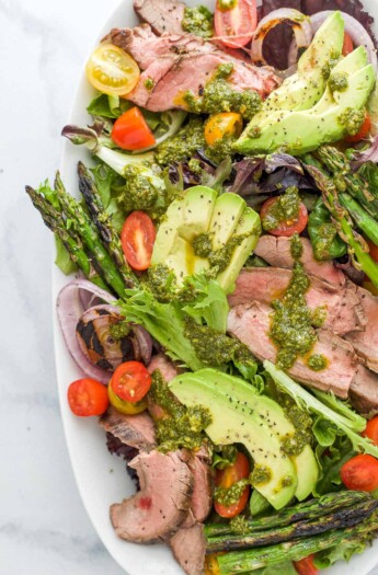 A platter of California steak salad topped with a drizzle of chimichurri dressing