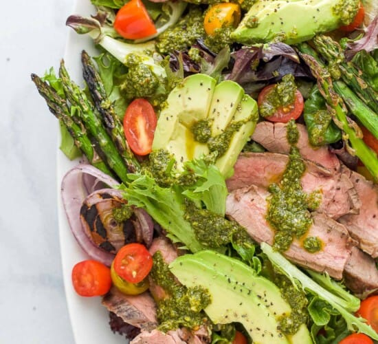 A platter of California steak salad topped with a drizzle of chimichurri dressing
