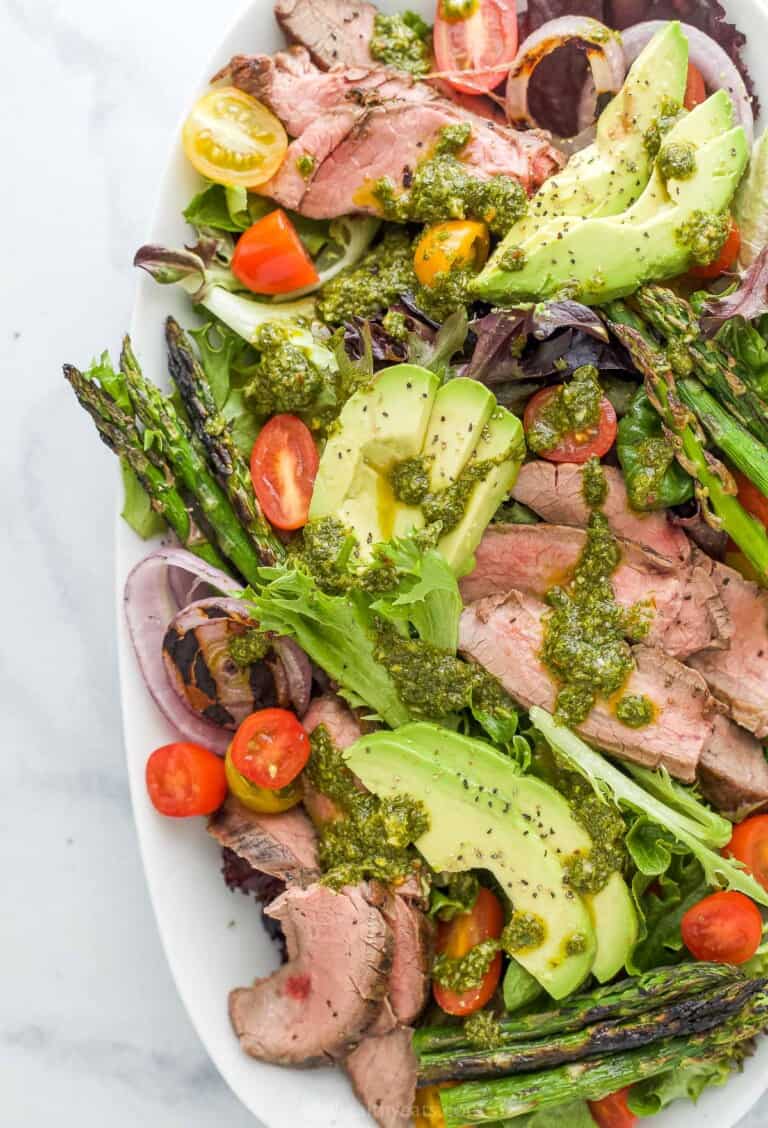 A platter of California steak salad topped with a drizzle of chimichurri dressing