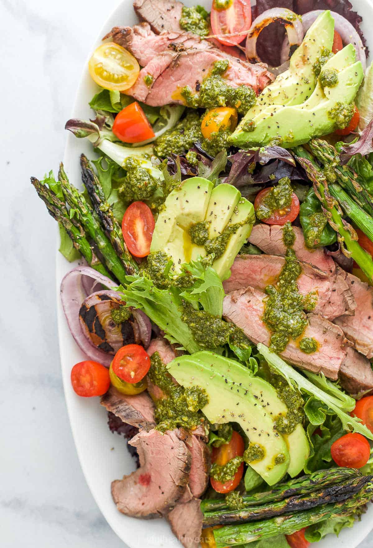 A platter of California steak salad topped with a drizzle of chimichurri dressing