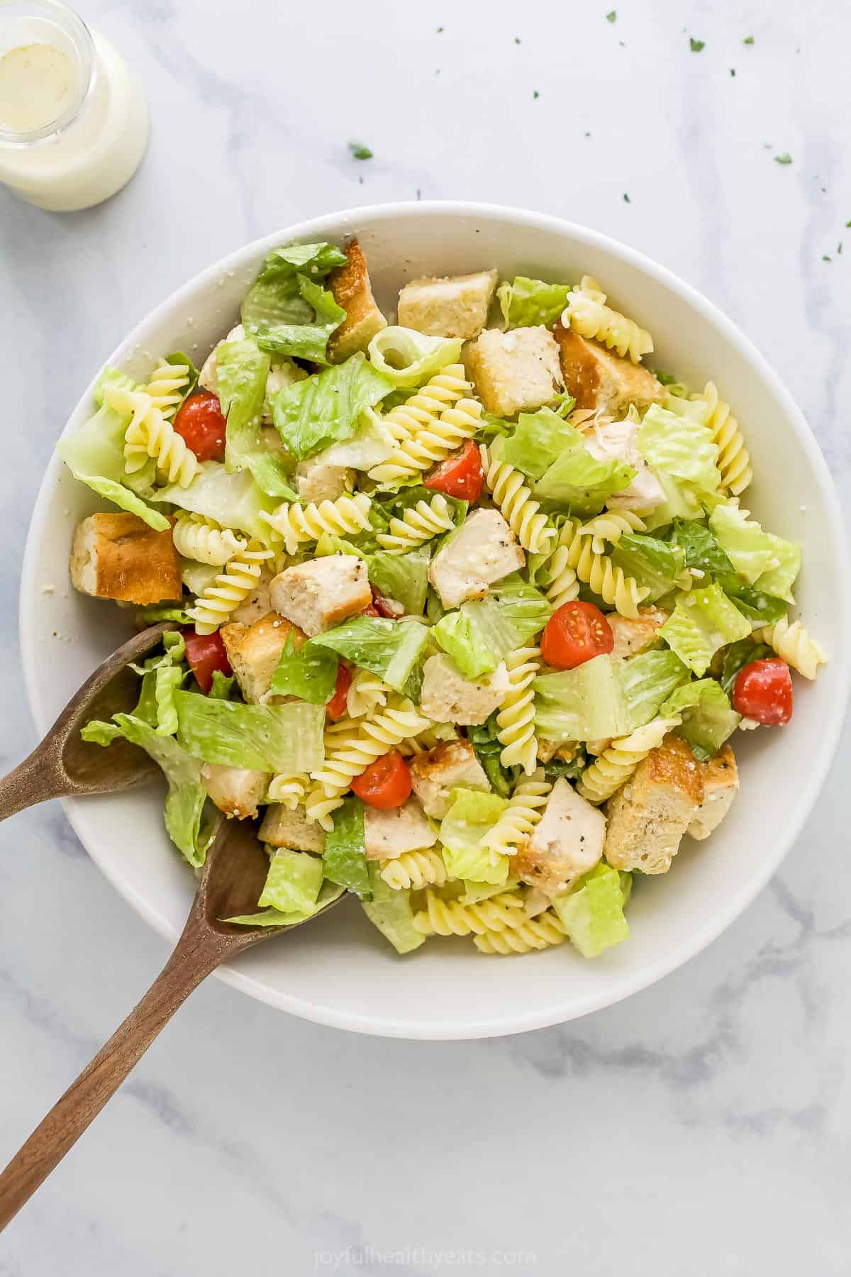 Two wooden spoons being used to toss a salad with caesar dressing