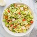 A homemade salad on a kitchen countertop beside a jar of dressing and a dish of grated parmesan