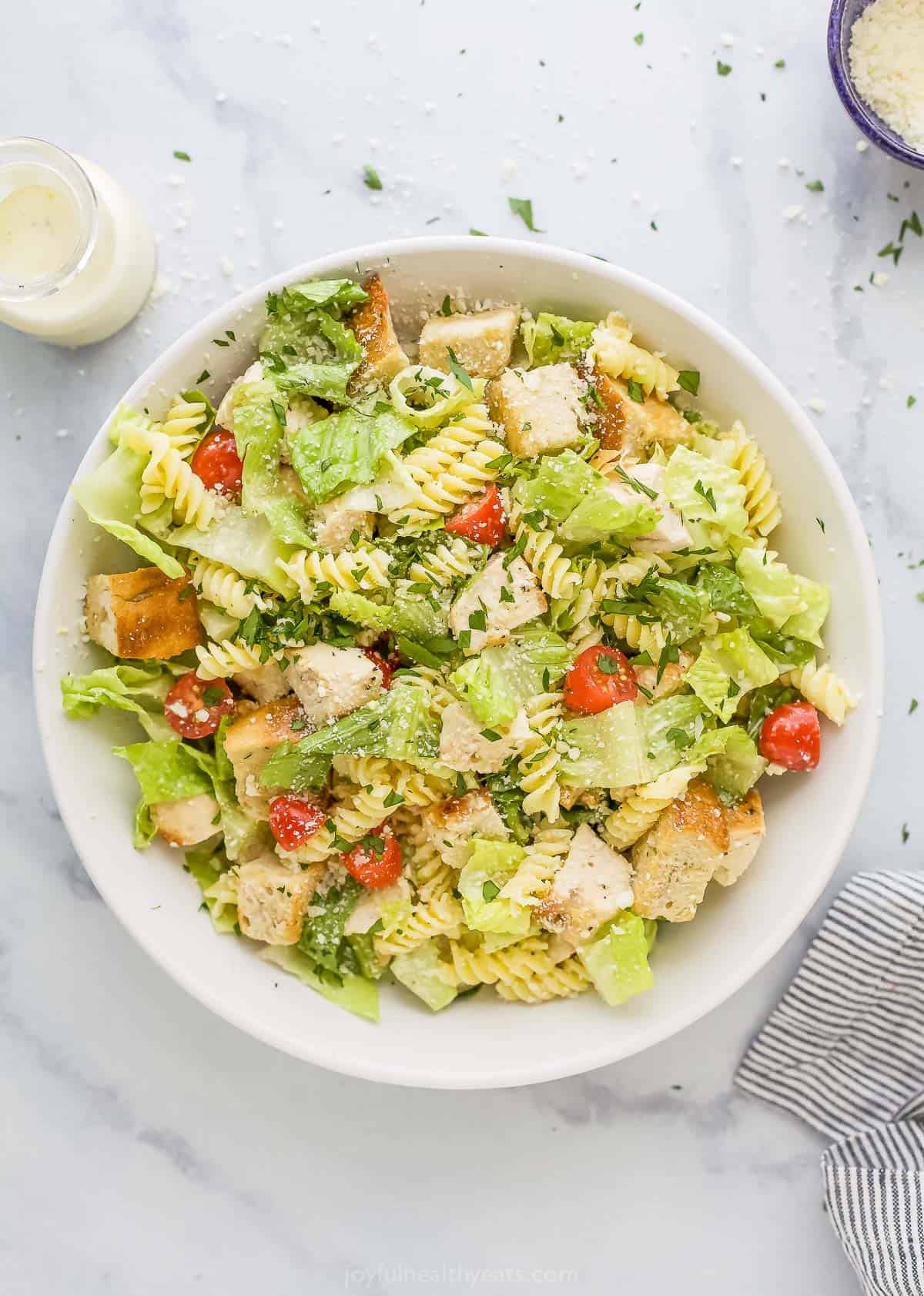 A homemade salad on a kitchen countertop beside a jar of dressing and a dish of grated parmesan