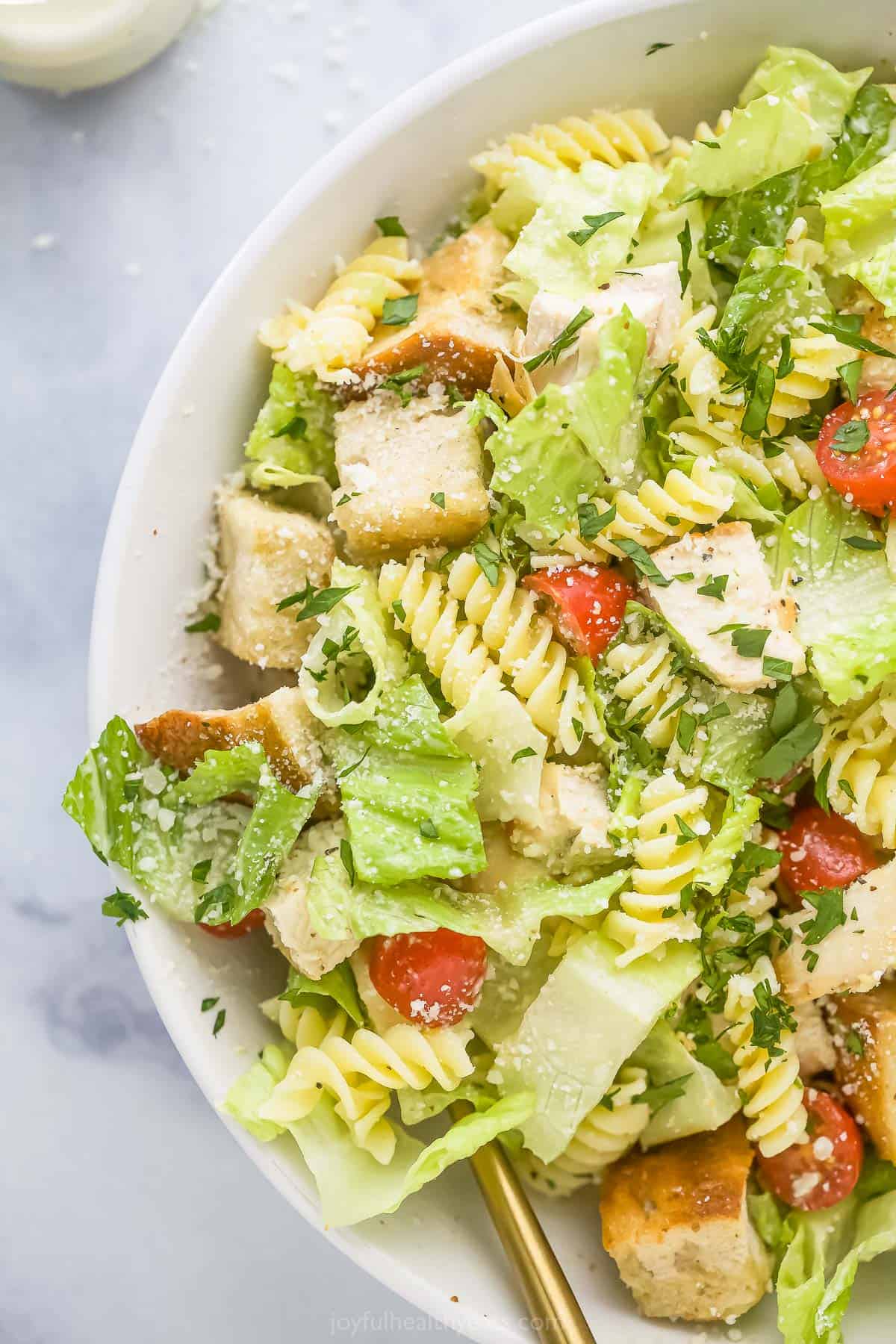 Chicken caesar pasta salad in a large white bowl on a marble surface