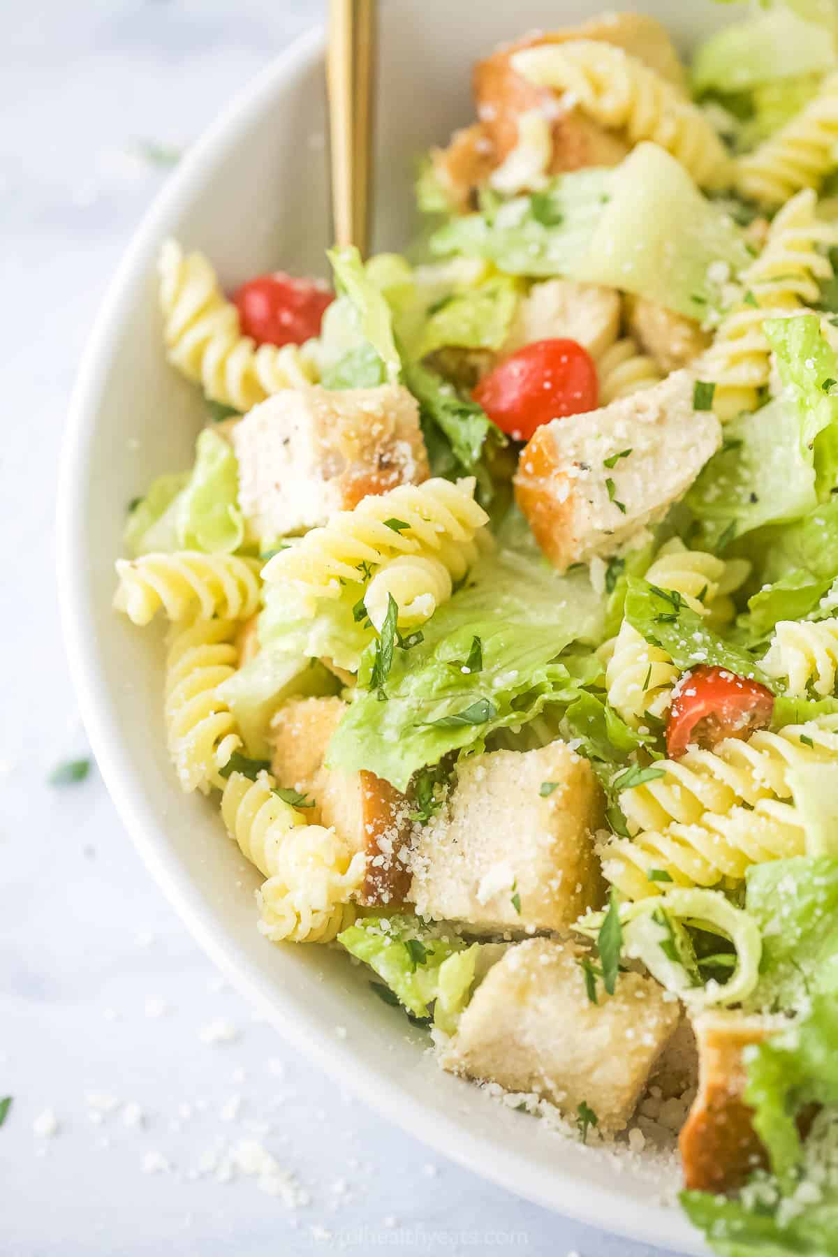 A close-up shot of a bowl of chicken caesar pasta salad on a kitchen countertop