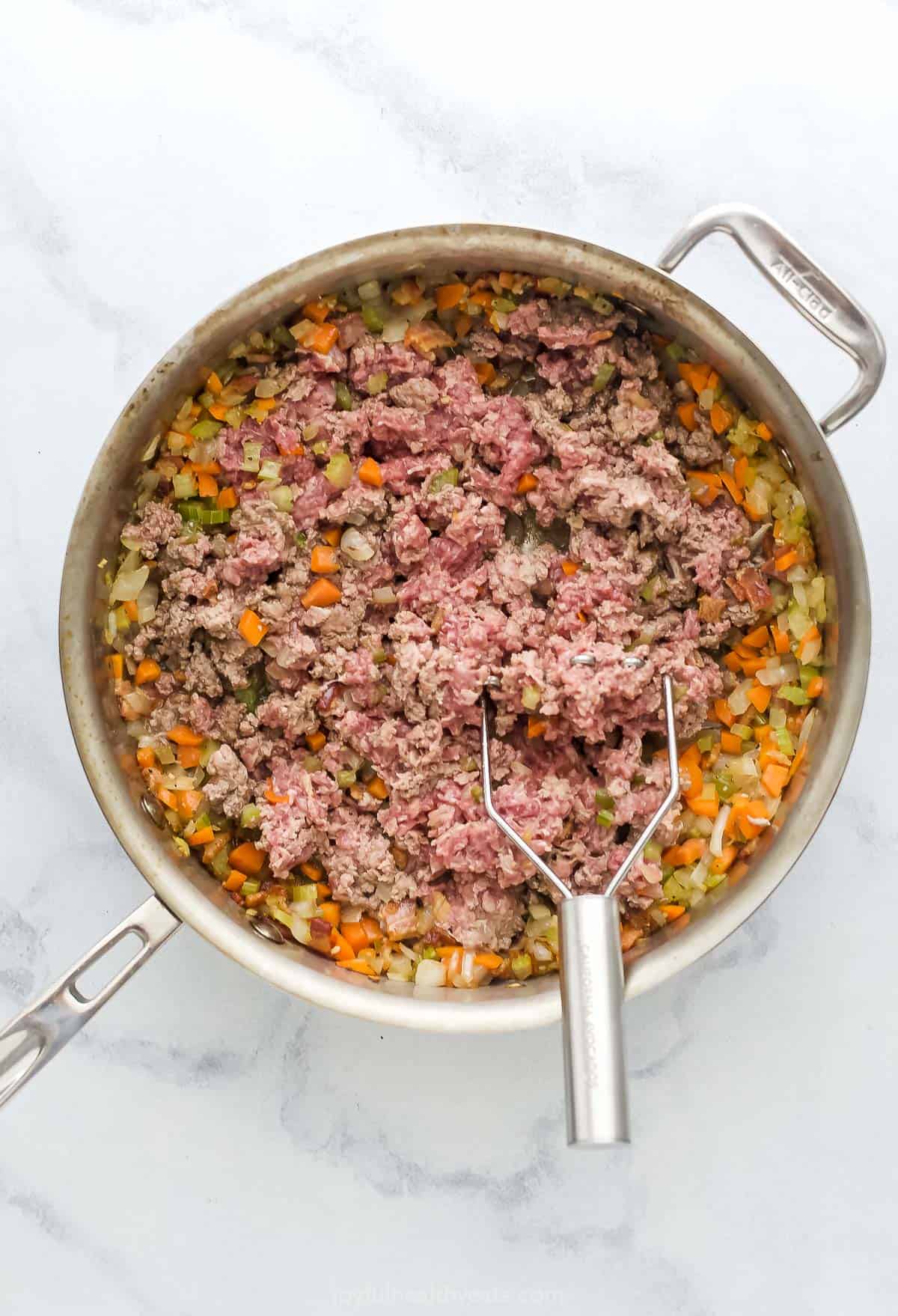 This Homemade Ragu Sauce is a quick version of an Italian staple. It's hearty and rich! The beef and tomato flavors develop in about one hour. Saute pan with ground beef being mashed up and mixed with cooked vegetables