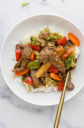 beef mixed with vegetables served on rice on a white plate