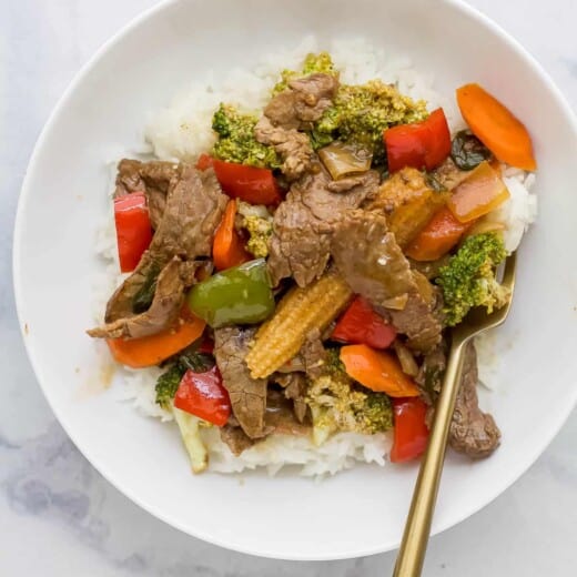 beef mixed with vegetables served on rice on a white plate