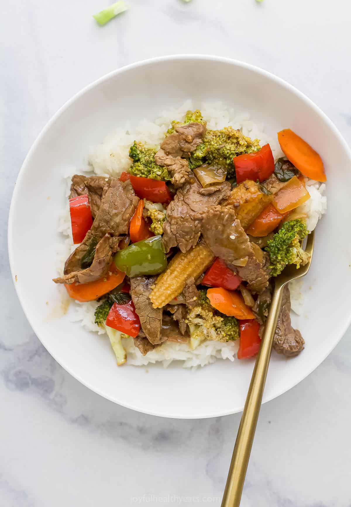 beef mixed with vegetables served on rice on a white plate