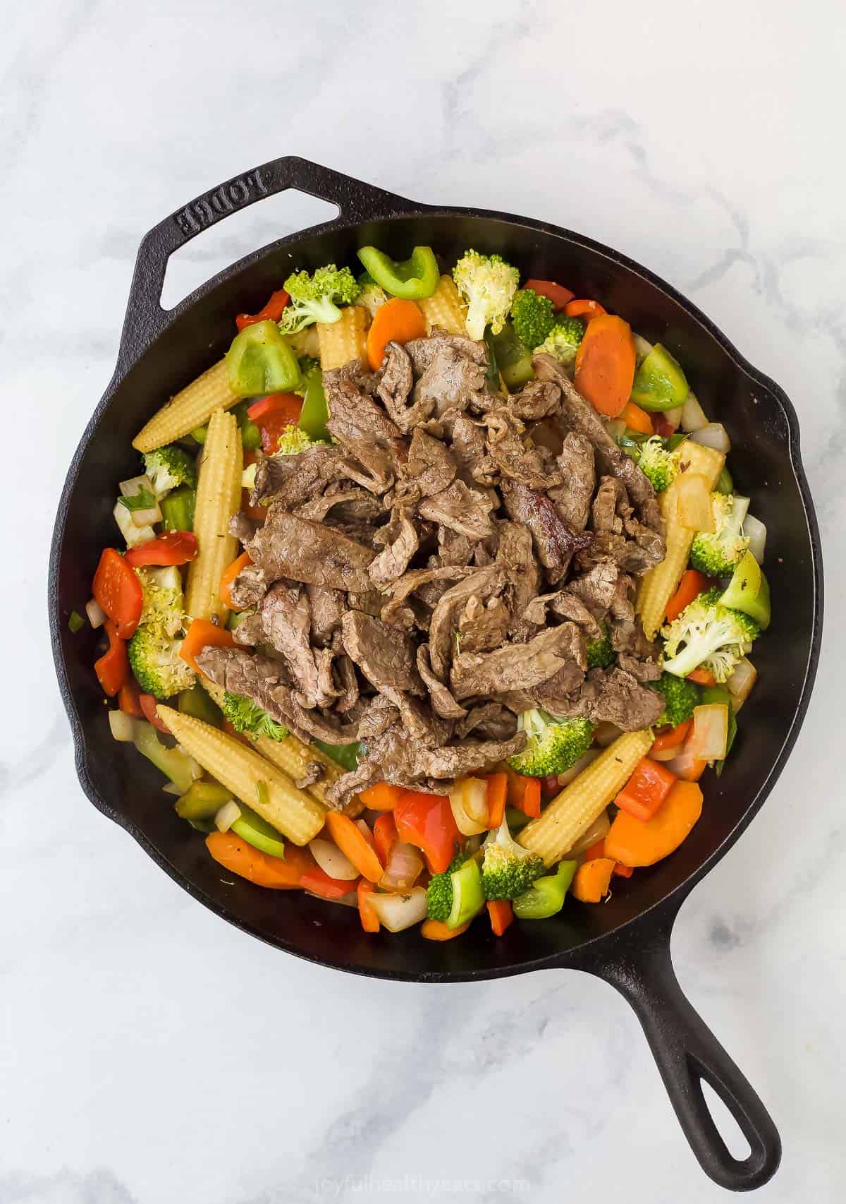 assorted chopped vegetables in a cast iron skillet with sliced cooked beef on top