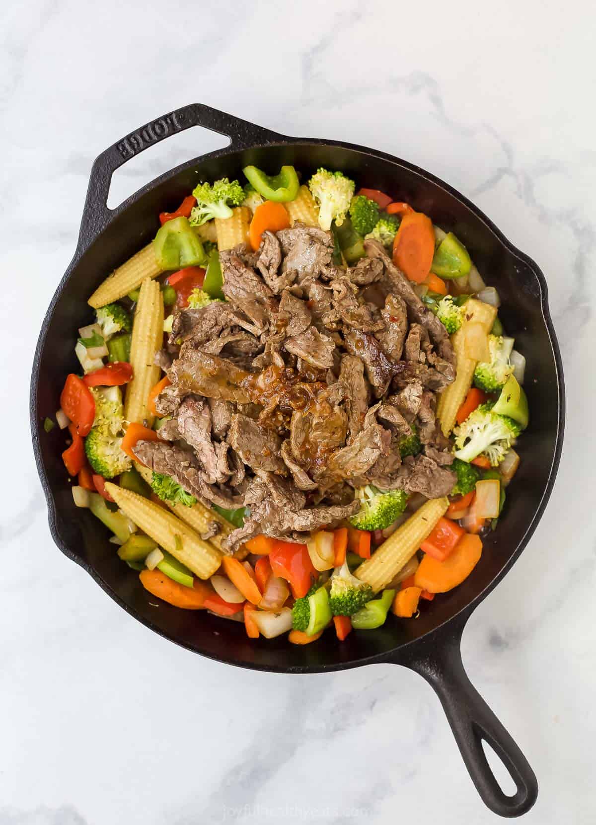assorted chopped vegetables in a cast iron skillet with sliced cooked beef on top