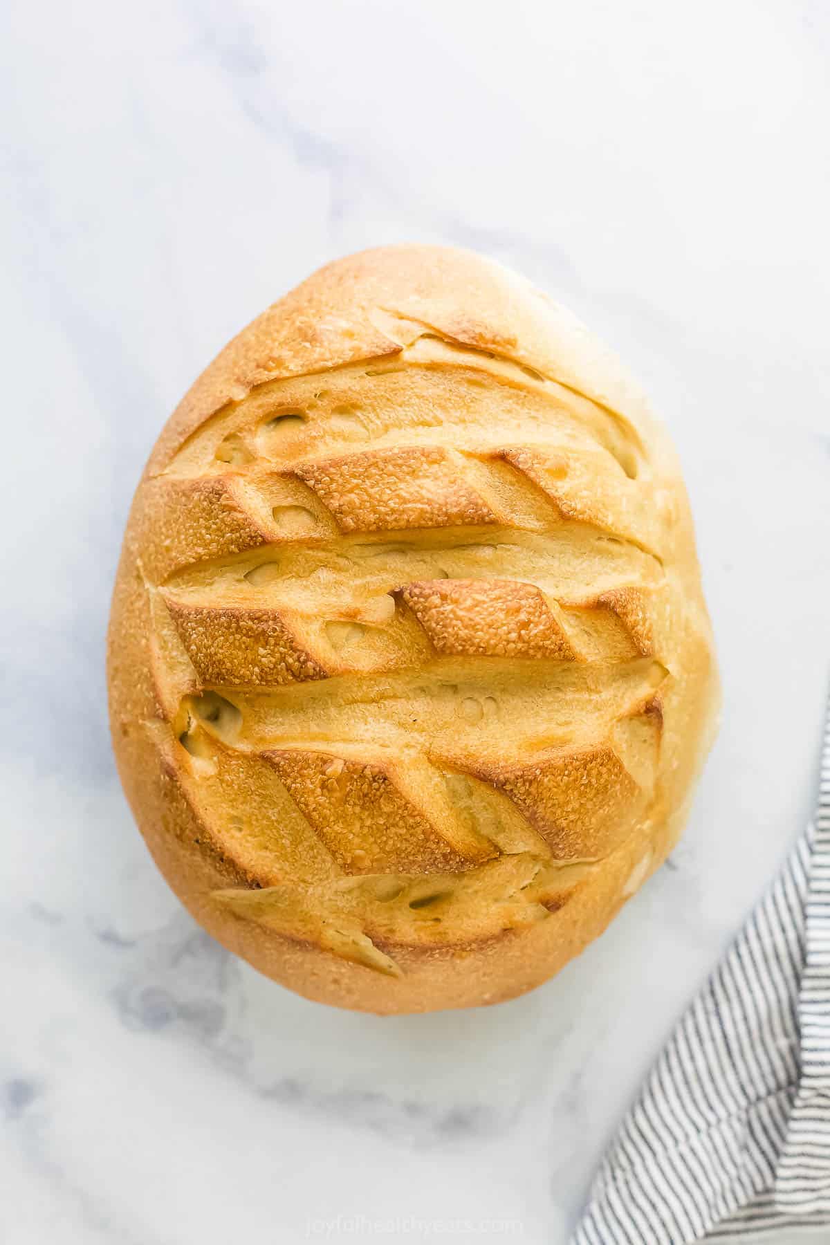 An artisan-style loaf of sourdough bread sitting on a countertop beside a dish towel