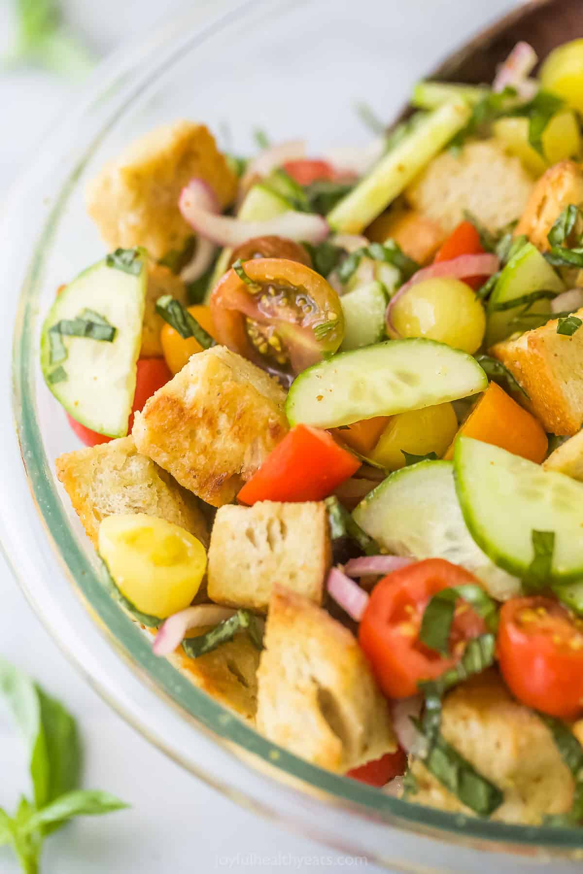 A close-up shot of a tomato panzanella salad inside of a large glass mixing bowl