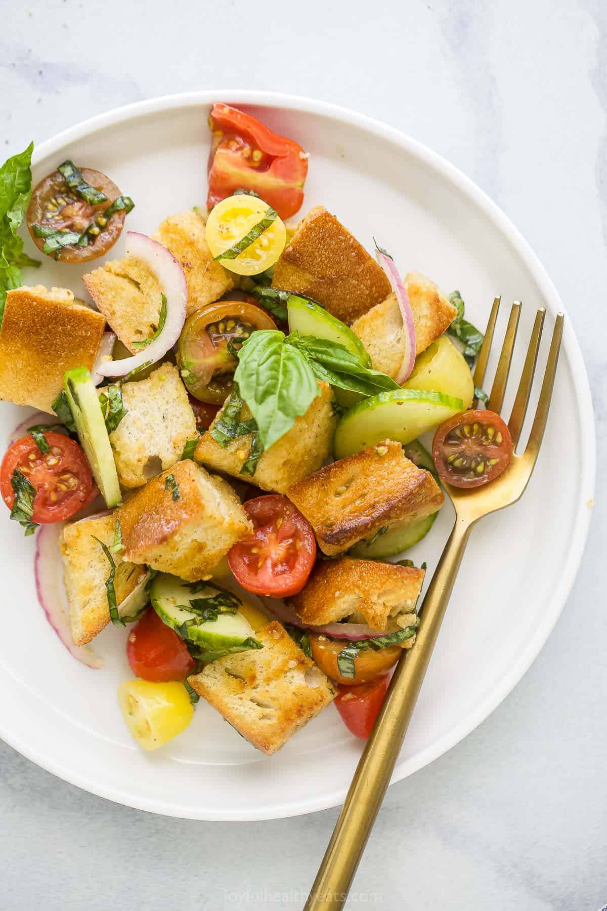 A plate of cucumber tomato onion salad with croutons and white balsamic vinaigrette dressing