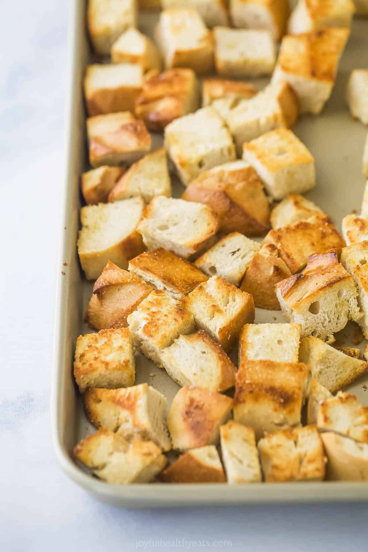 A close-up shot of homemade croutons on a metal baking sheet with a raised rim
