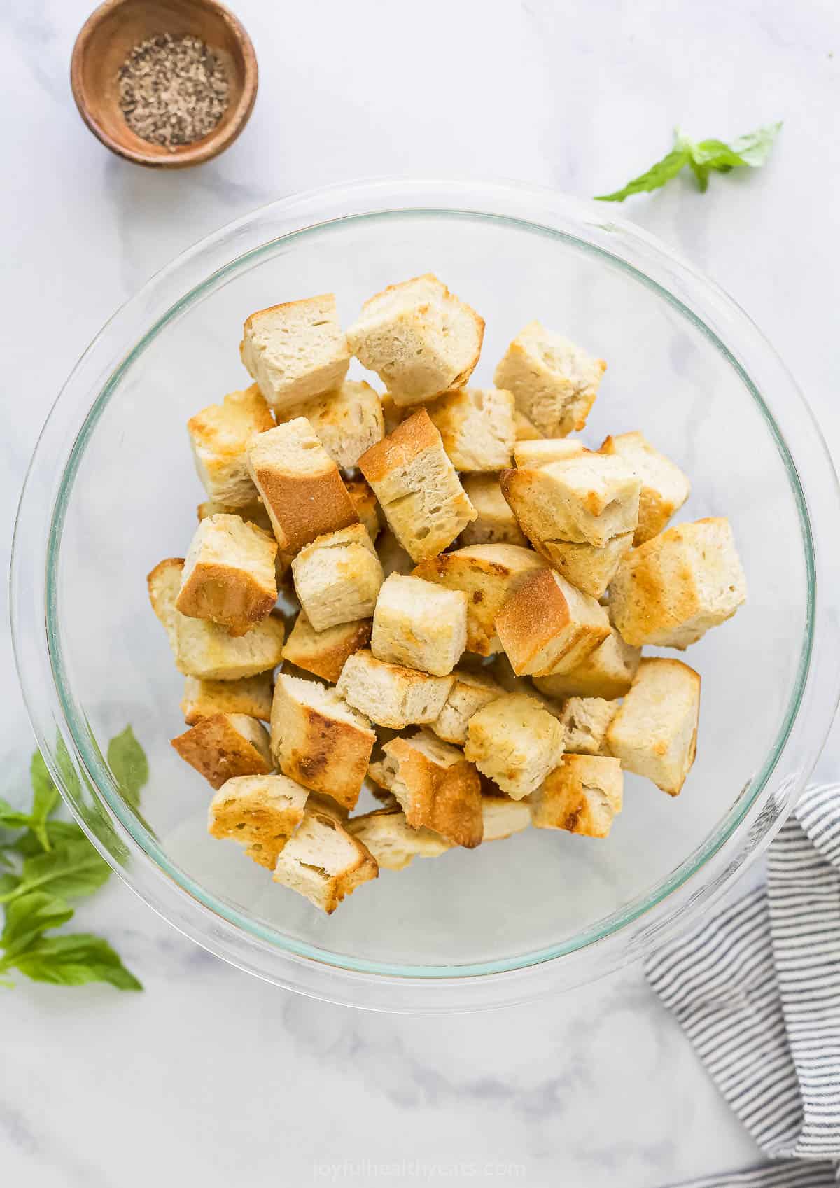 Homemade garlic croutons in a big clear bowl on a marble countertop