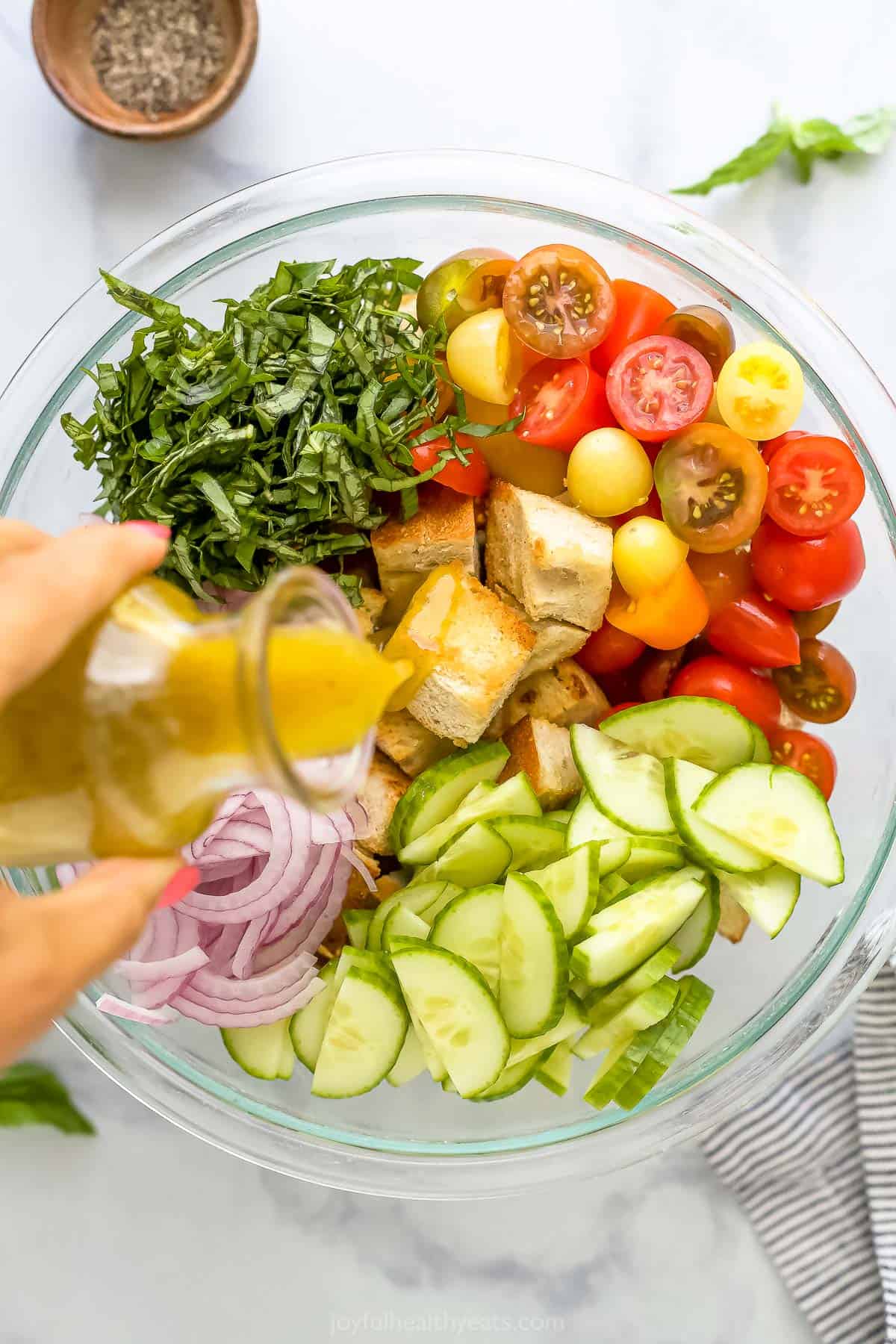 White balsamic vinaigrette dressing being poured over a bowl full of croutons, veggies and basil