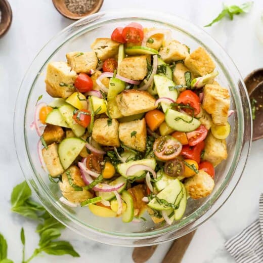 Tomato panzanella salad in a bowl on a kitchen countertop beside spices and fresh herbs