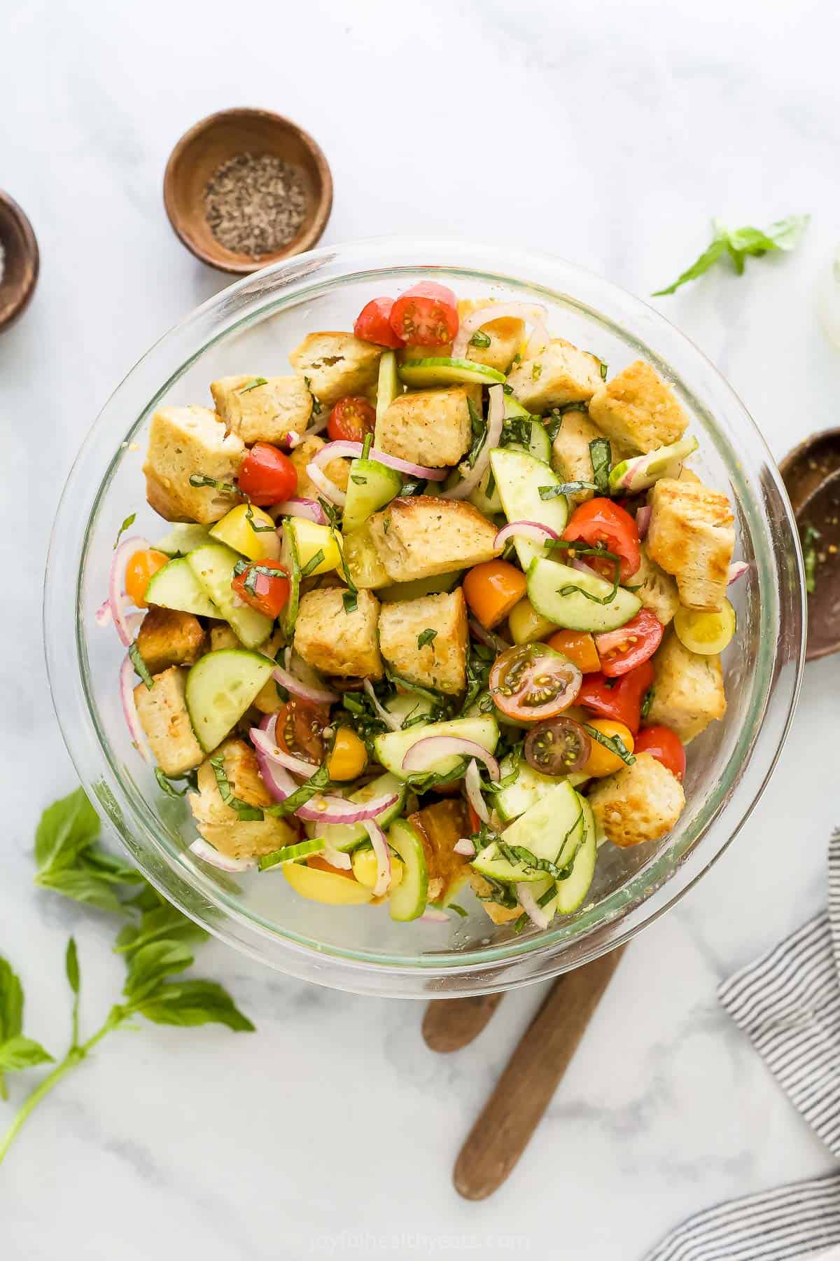 Tomato panzanella salad in a bowl on a kitchen countertop beside spices and fresh herbs