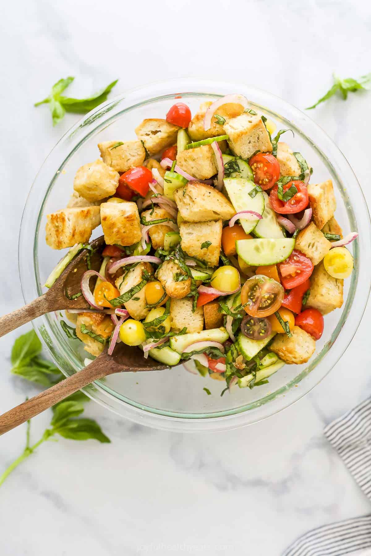 A bowl full of tomato panzanella salad with two wooden spoons being used to toss it