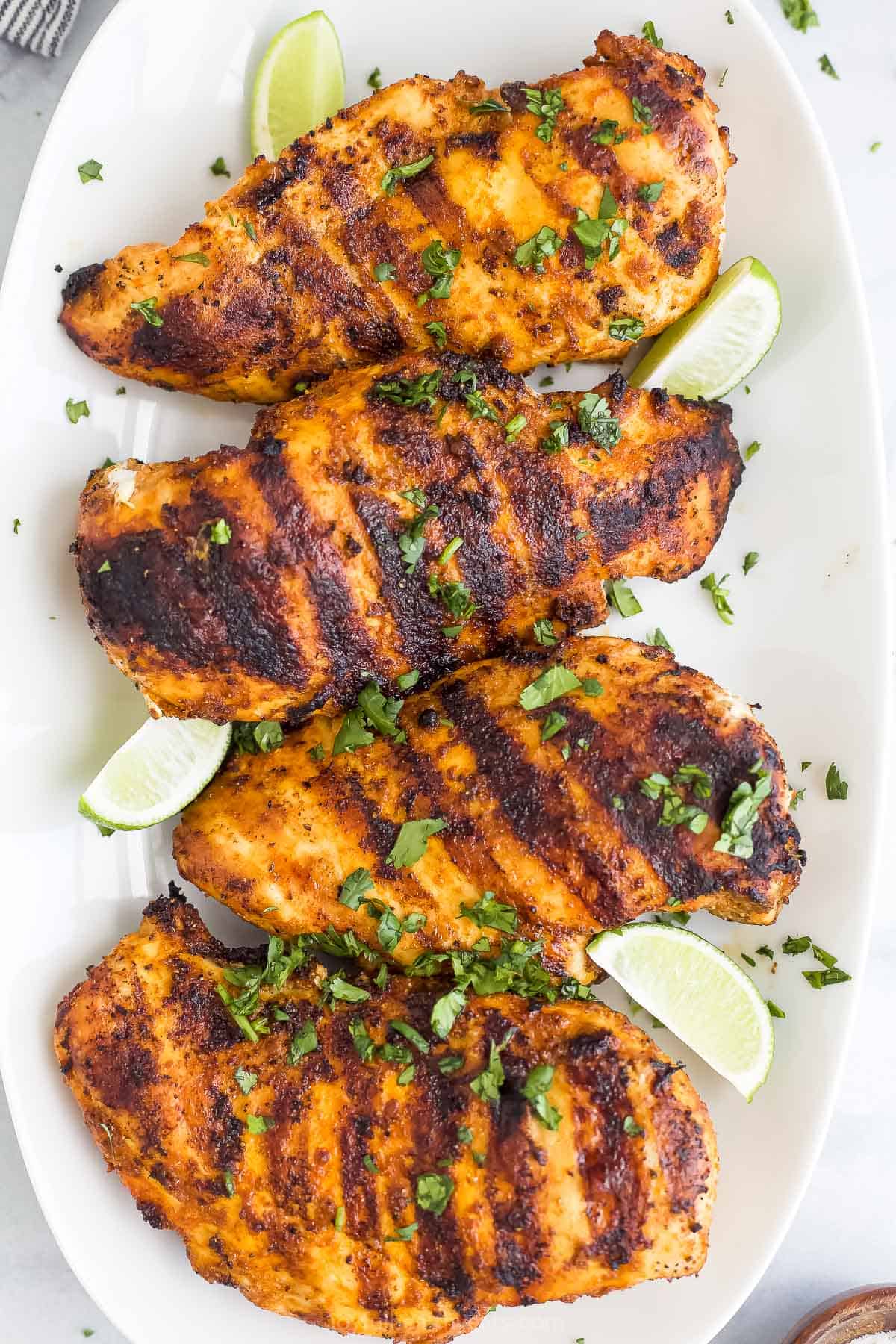 Four boneless, skinless breasts with sear marks on a serving platter with four fresh lime wedges