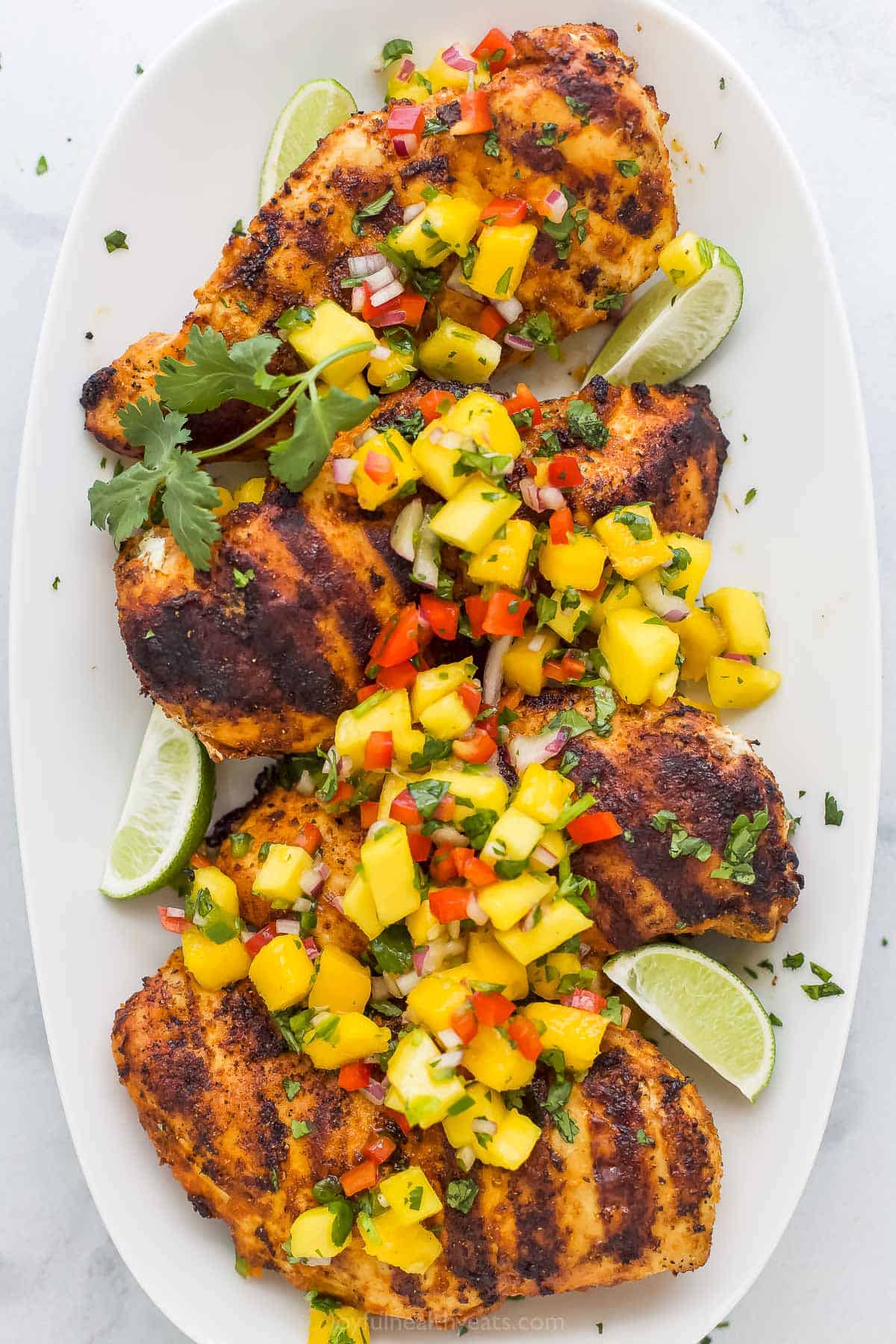 Four grilled chicken breasts on a serving platter with mango salsa spooned over them