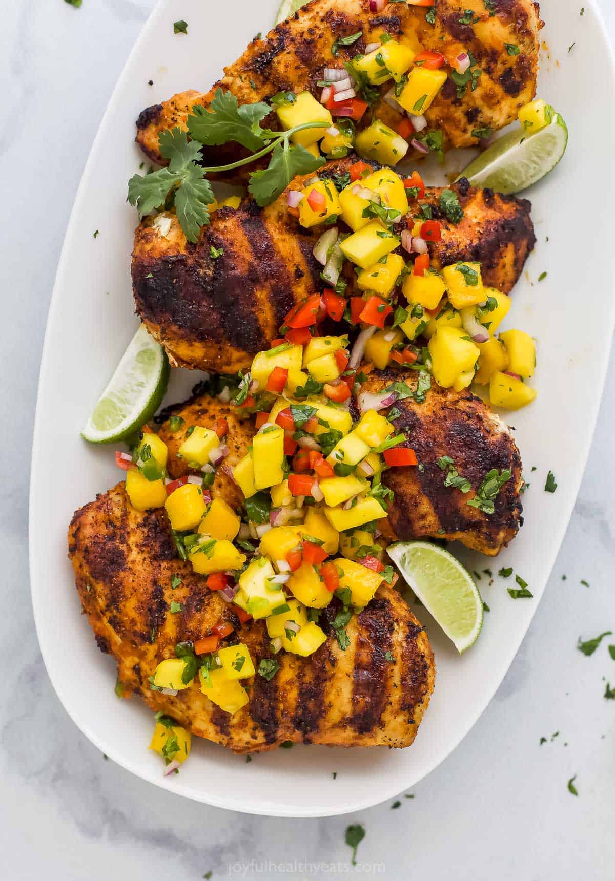 A serving platter filled with grilled mango chicken on a kitchen countertop