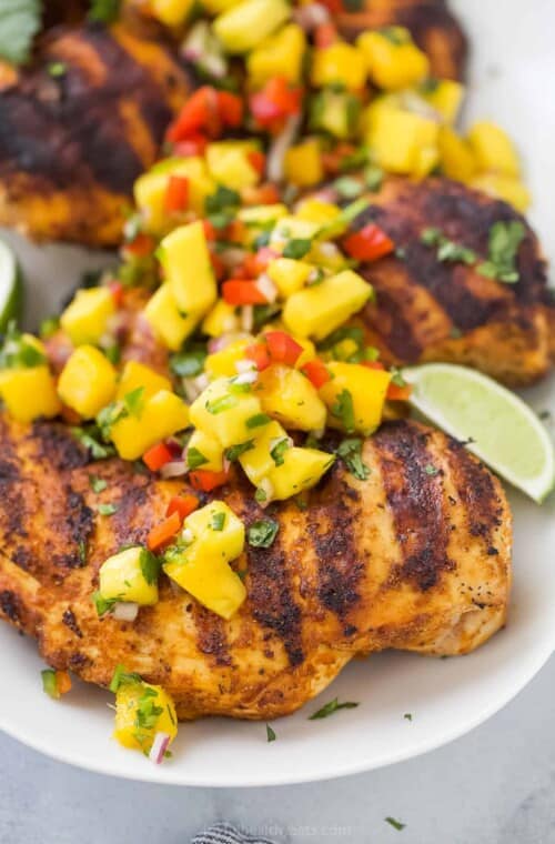 A close-up shot of grilled mango chicken on a platter with fresh lime wedges