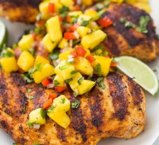 A close-up shot of grilled mango chicken on a platter with fresh lime wedges