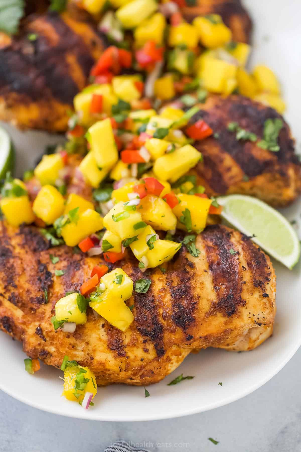 A close-up shot of grilled mango chicken on a platter with fresh lime wedges