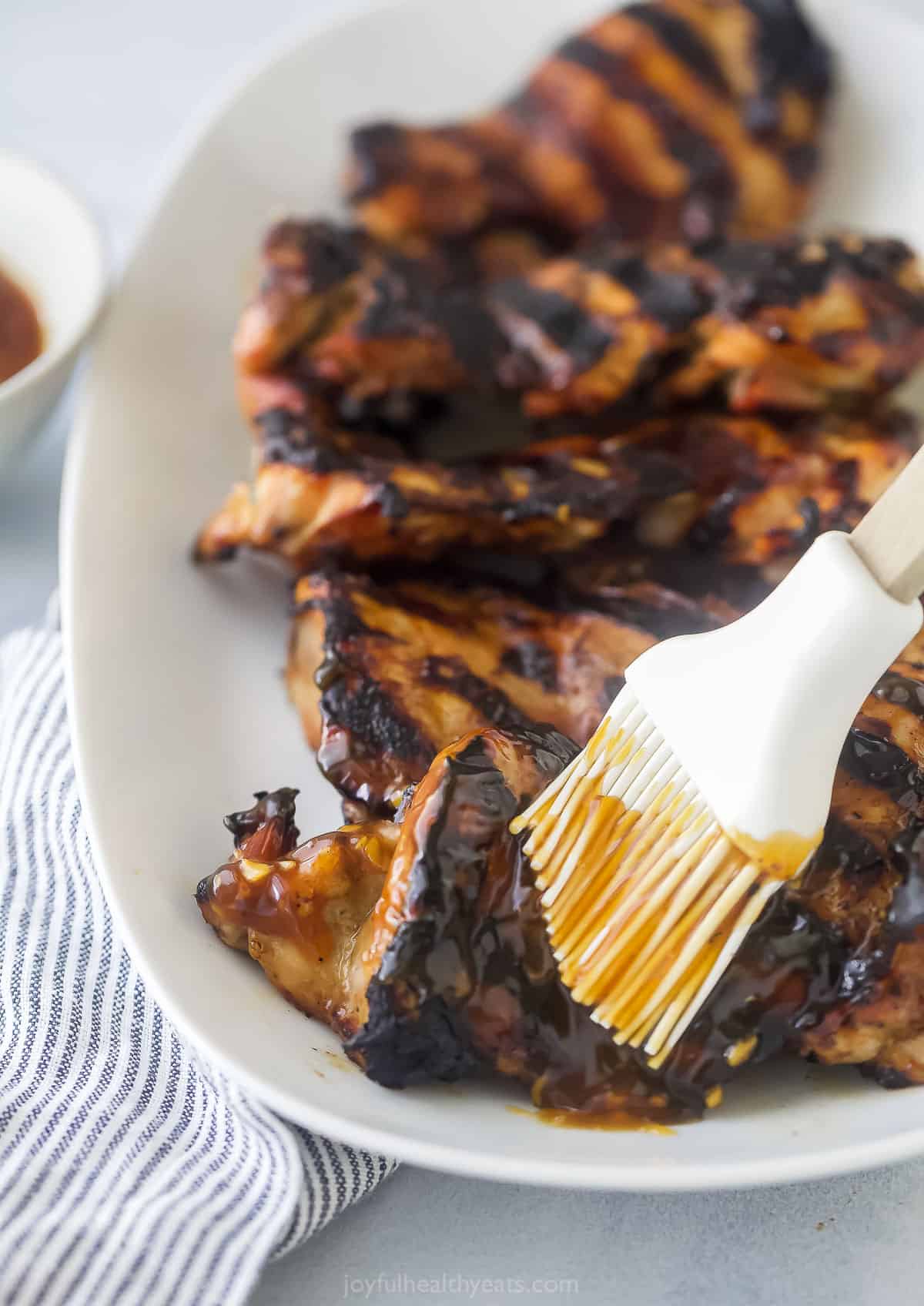 Freshly grilled chicken thighs being rubbed with homemade teriyaki sauce