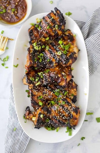 A platter full of teriyaki grilled chicken thighs on top of a striped kitchen towel