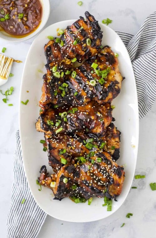A platter full of teriyaki grilled chicken thighs on top of a striped kitchen towel