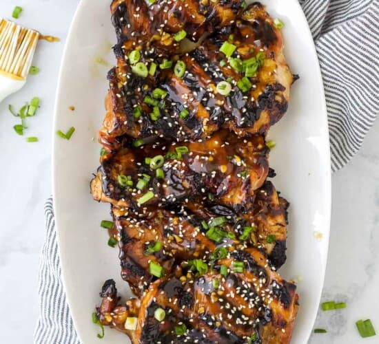 A platter full of teriyaki grilled chicken thighs on top of a striped kitchen towel