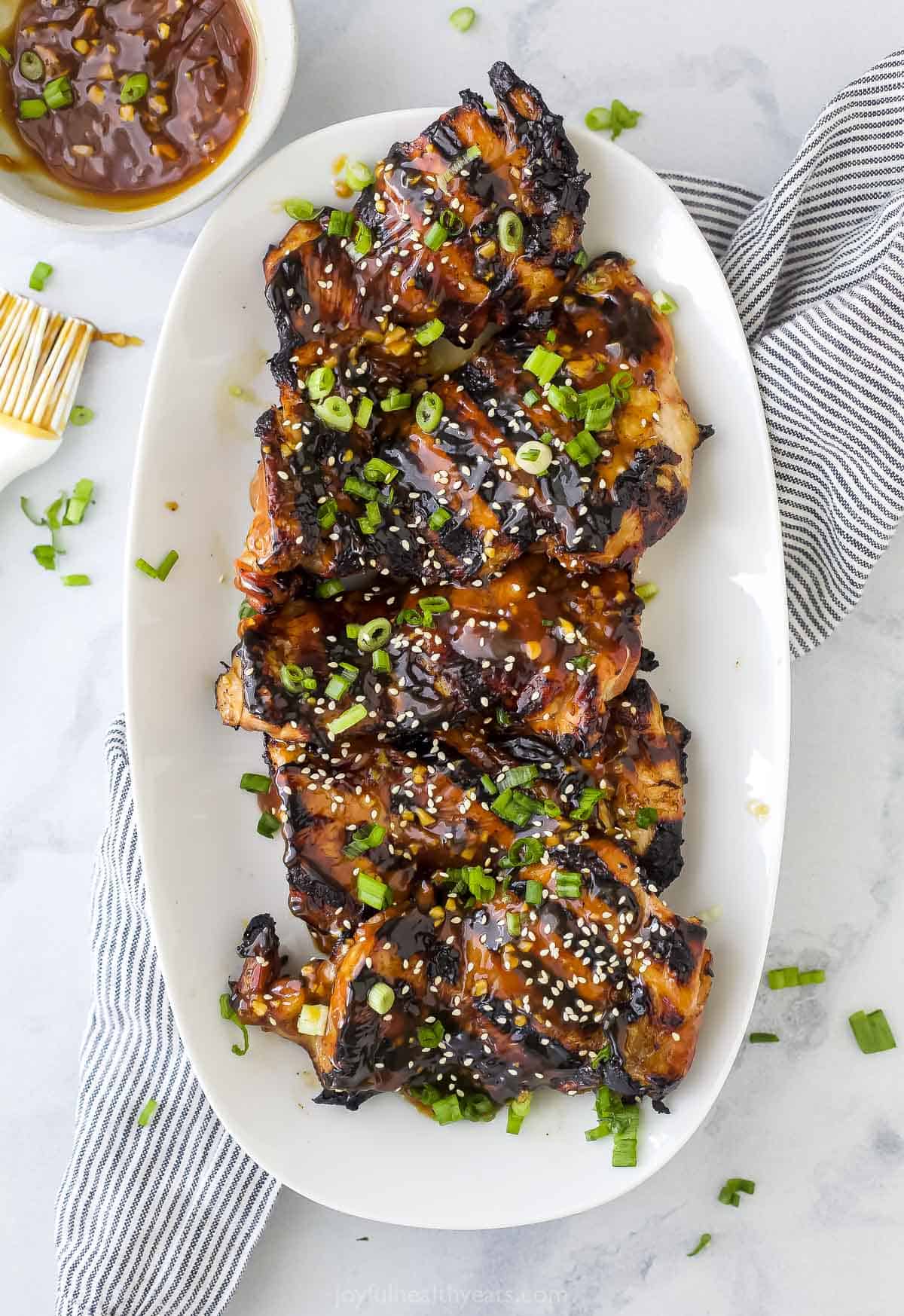A platter full of teriyaki grilled chicken thighs on top of a striped kitchen towel